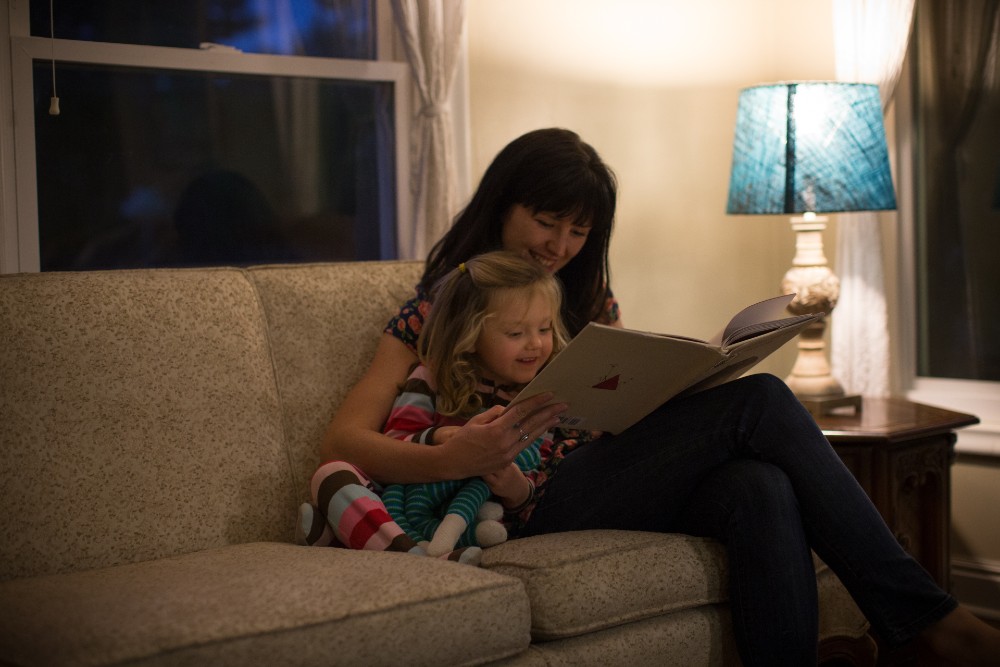 A mother and daughter reading a picture book by lamplight.