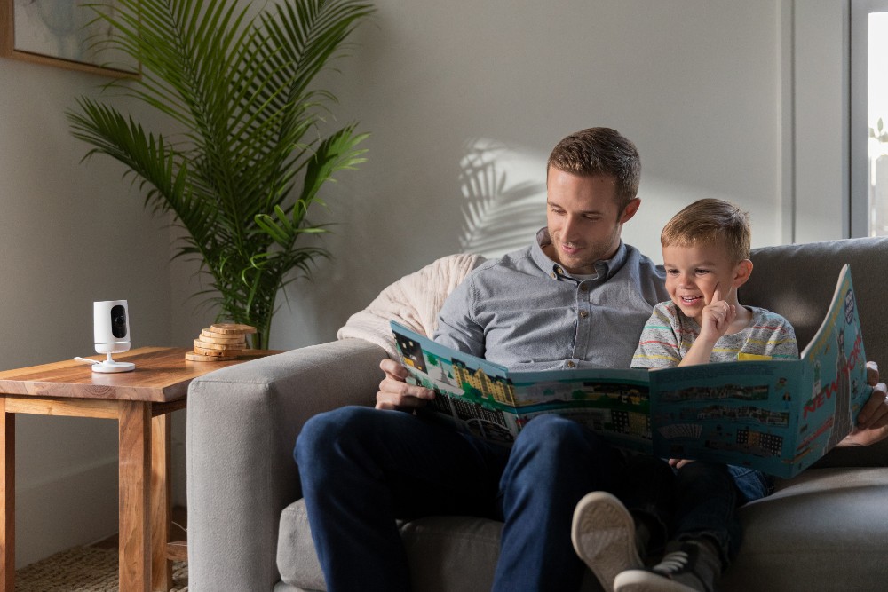 Father and son reading on a couch with a Vivint Indoor Security Camera on the side table.