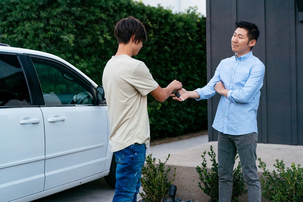 Teenage son handing his smiling father the car keys.