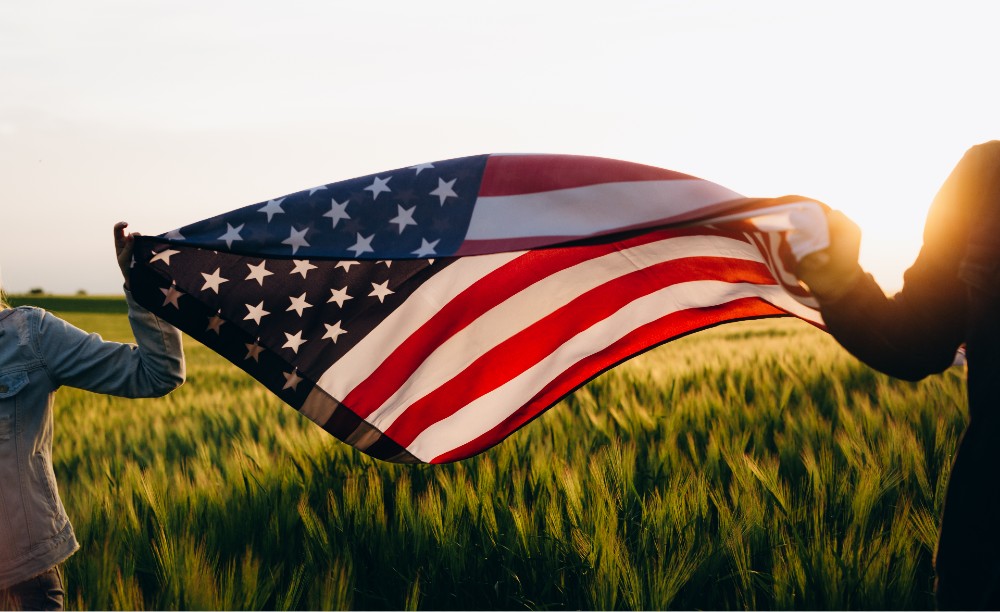 An American flag held by two people billowing in the wind.