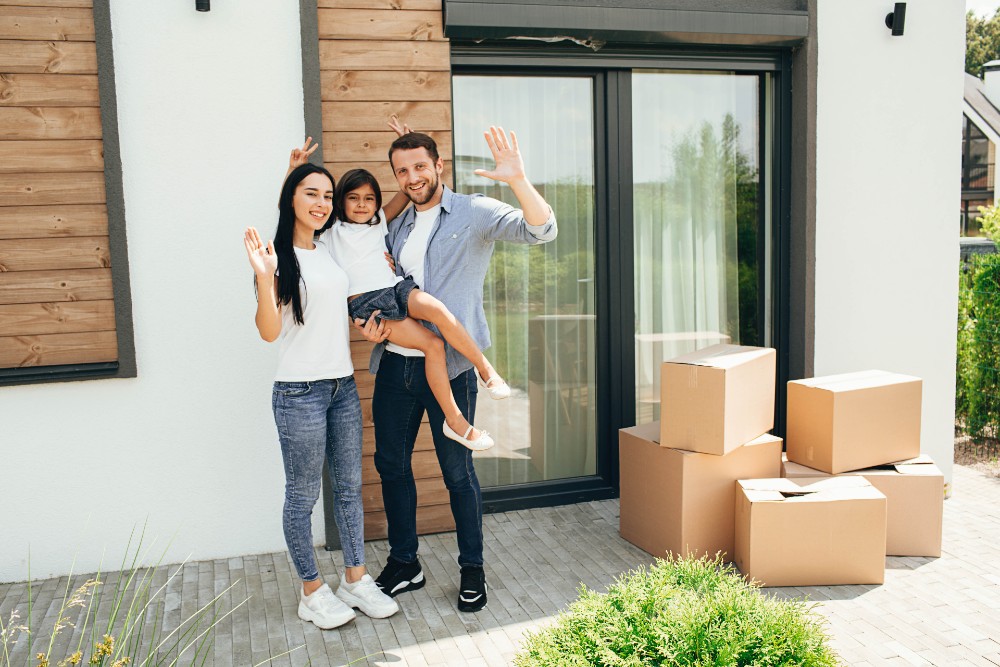 Two parents and their young daughter standing in front of their new house.