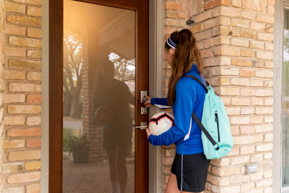 A teenager getting home from soccer practice letting herself in through the smart door lock.