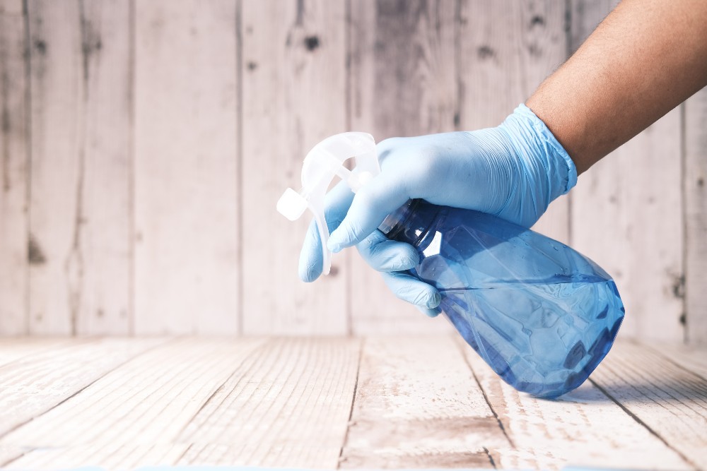 Gloved hand spraying disinfectant on a table.