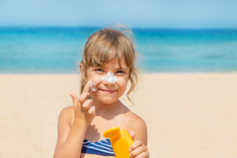 Young girl applying sunscreen to her face at the beach.