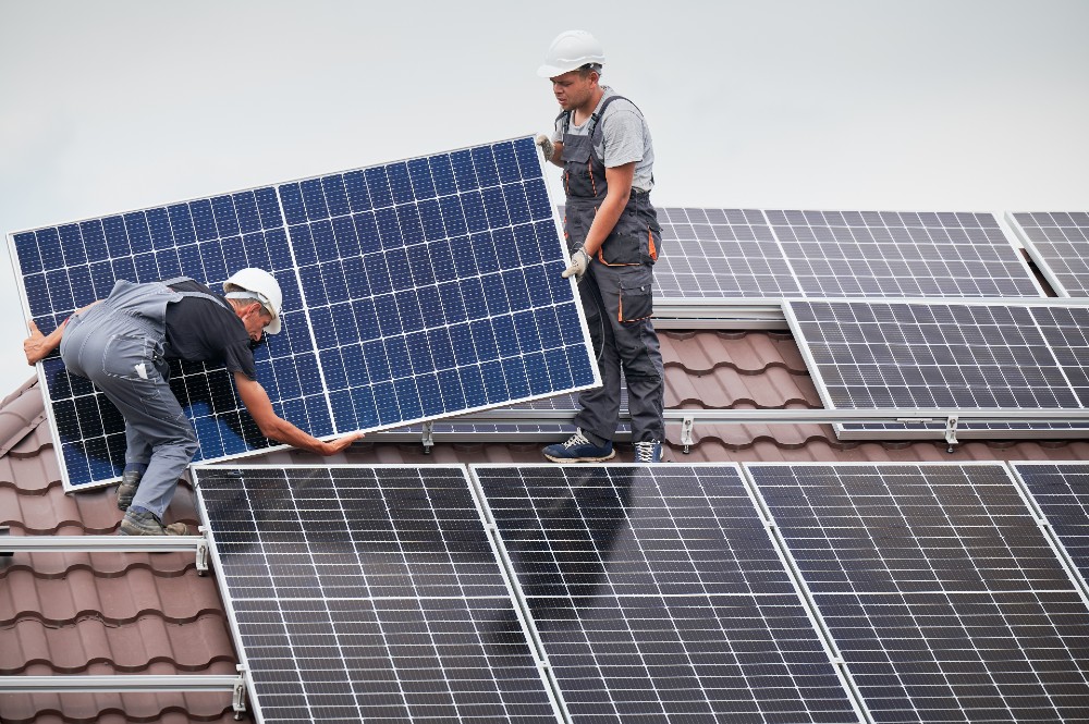 Two workers installing solar panels on a home's roof.