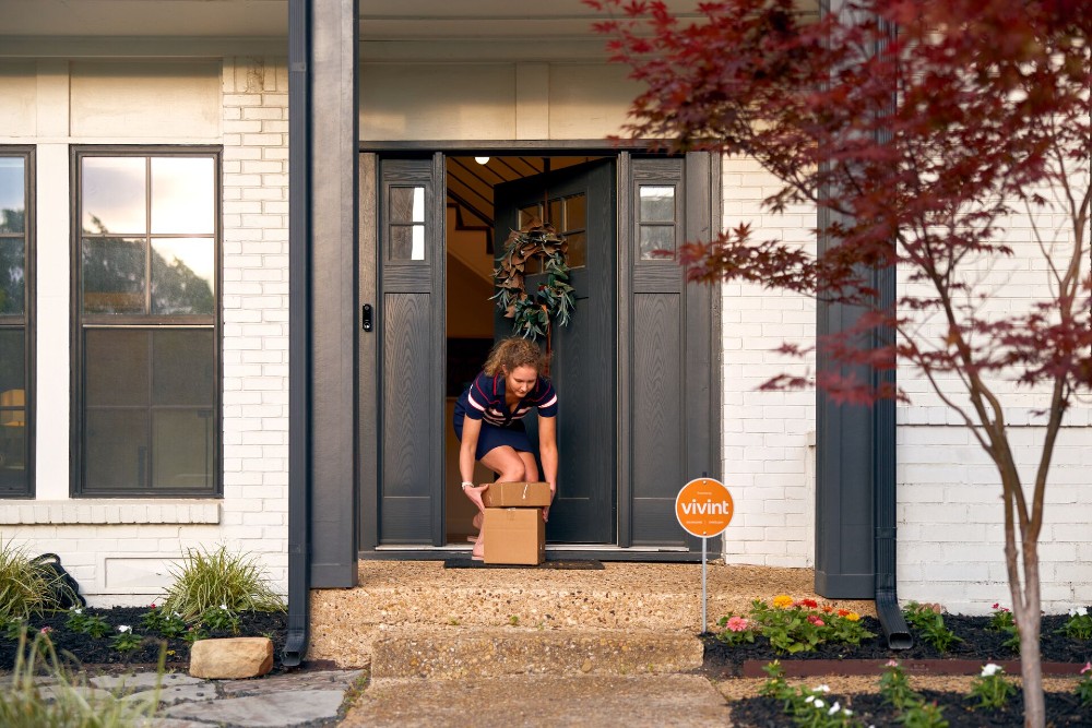 Woman opening her front door and picking up a package from her porch.