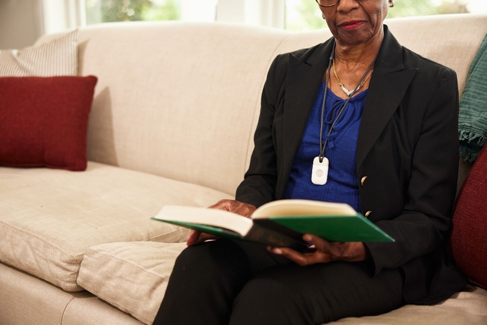Woman reading a book and wearing a Vivint emergency pendant.