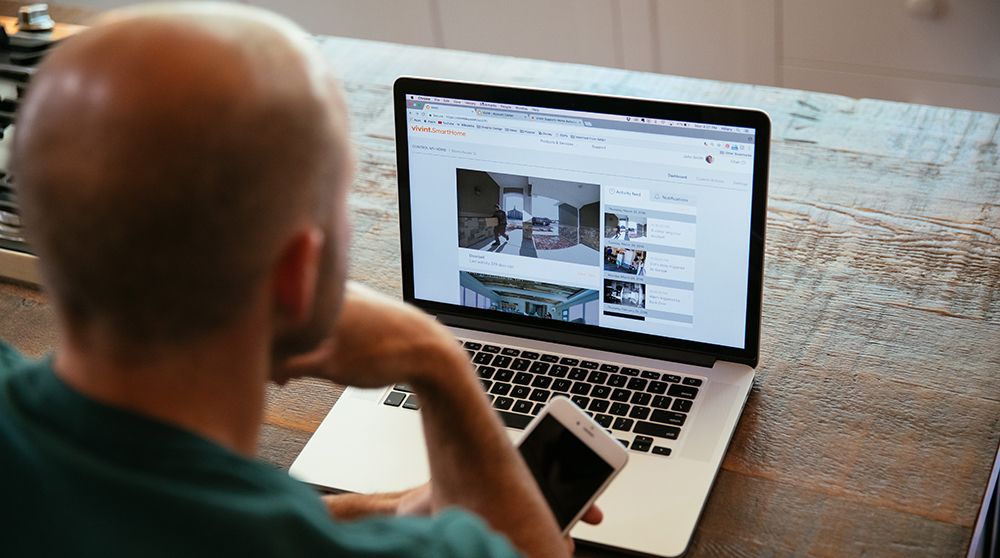 A man monitors a package delivery via a doorbell camera feed on his laptop